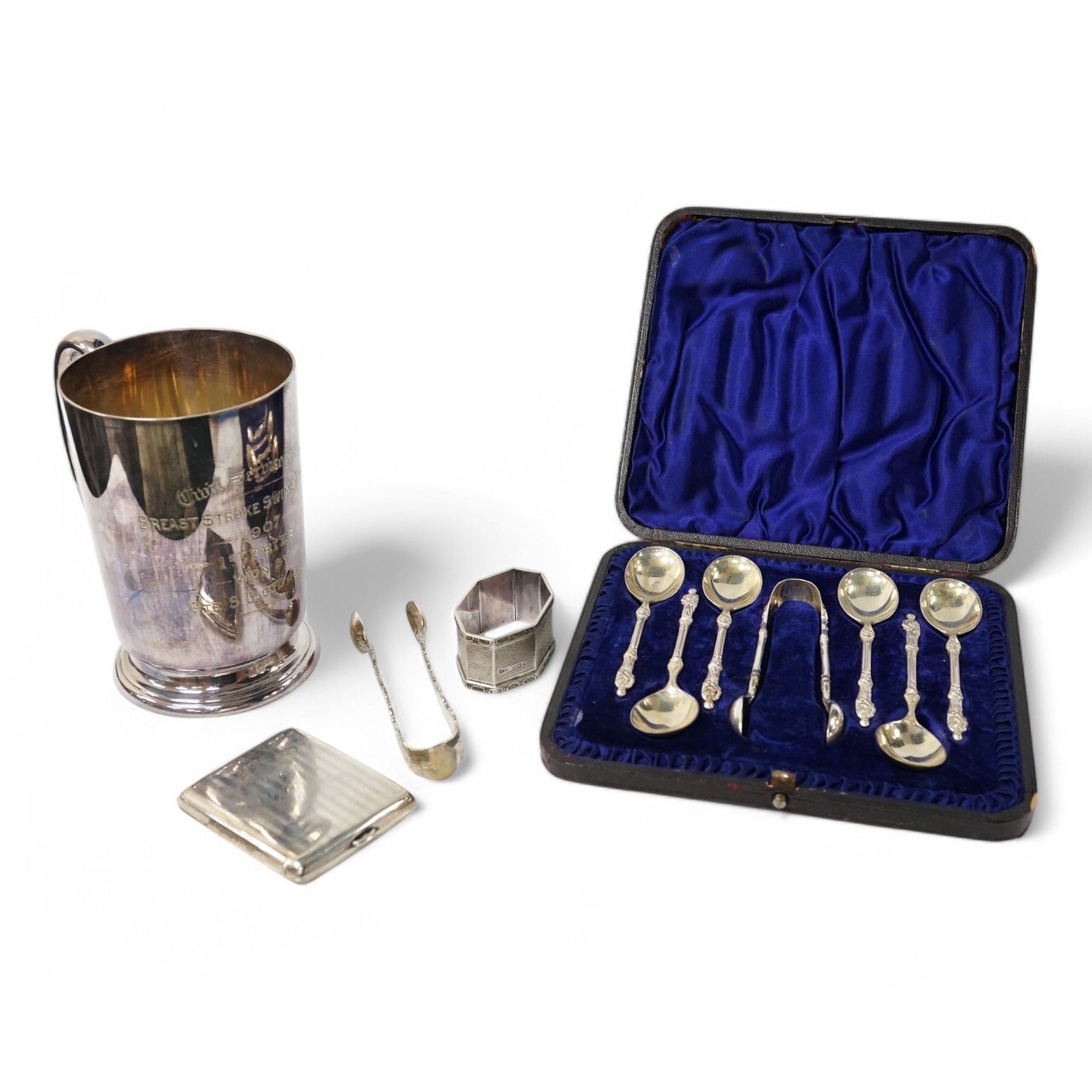 A George V silver mounted brass cased travelling timepiece, London, 1916, 70mm, together with a silver napkin ring, a pair of silver sugar tongs, a cased set of silver Victorian silver teaspoons with sugar tongs and a pl